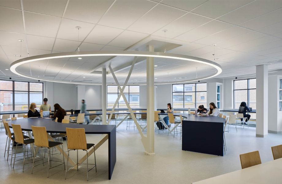 Rotonde avec longue tables en stratifié, chaises en bois, gros luminaire suspendu et étudiants