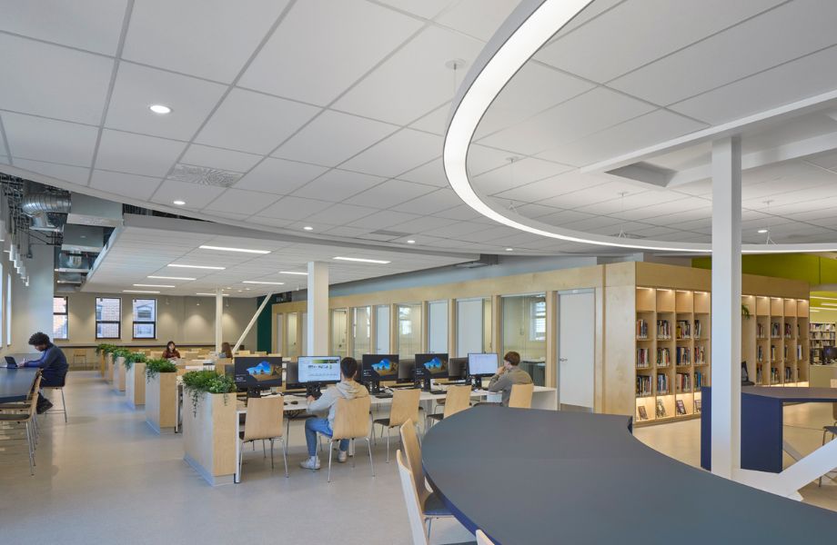 Longues tables blanche avec chaises en bois, plantes et étudiants à l'ordinateur