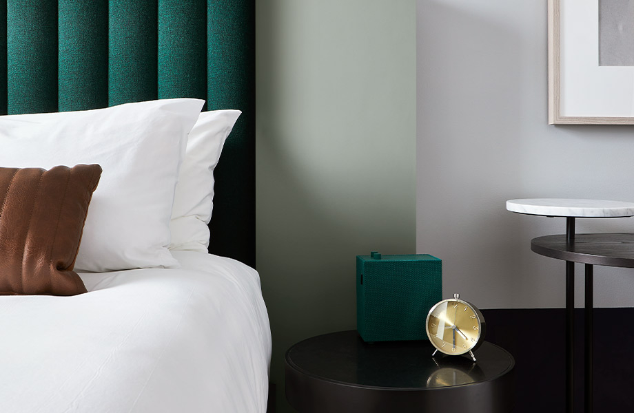 Hotel room with white bedding, dark green headboard, nightstand with clock, and feature wall in FENIX J0794 Verde Kitami 