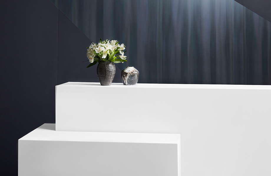 Luna Brite White Everform Solid Surface reception desk with computer and flowers in front of Dark Rolled Oil Steel Homapal Metal Laminate and Nocturne Formica Laminate wall
